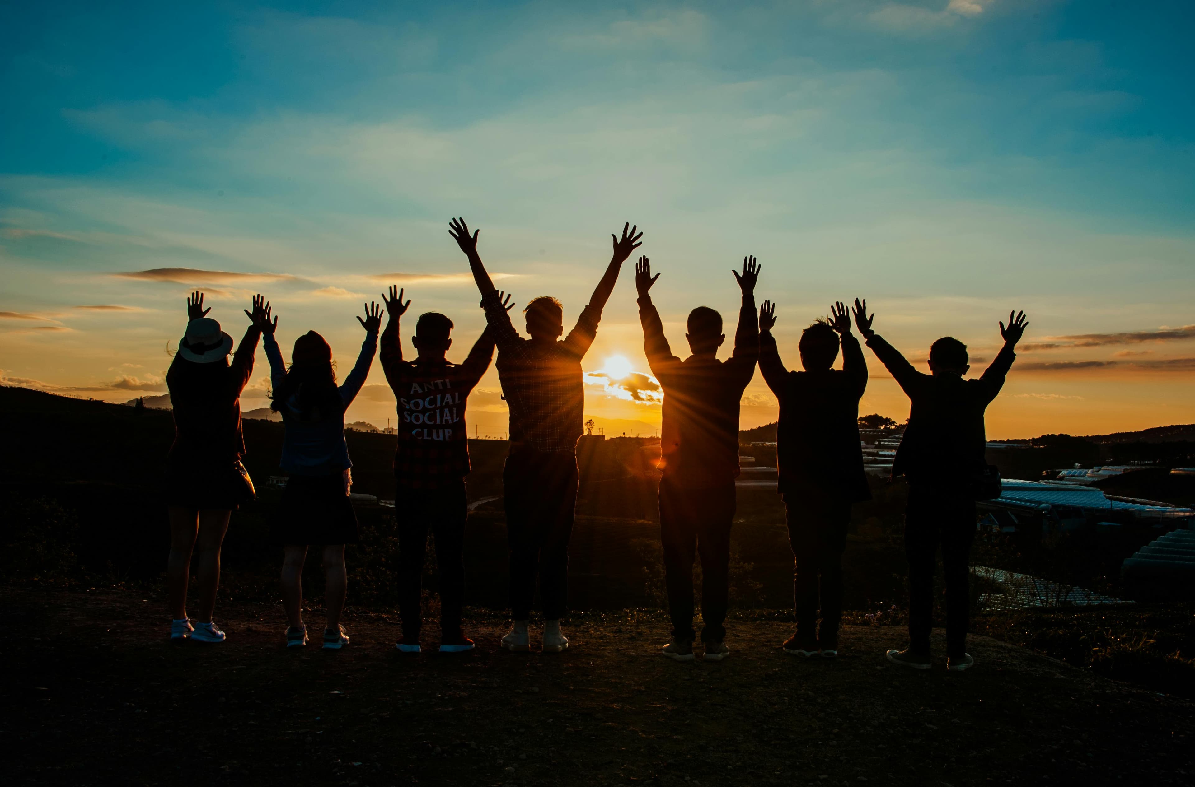 Silhouette of people raising their hands together.